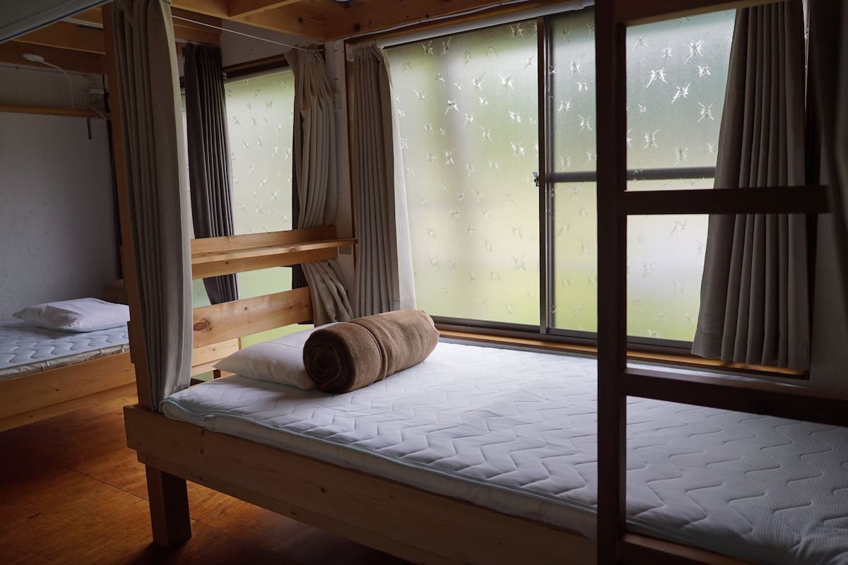Quarto com beliche, janela, cortinas e colchão.