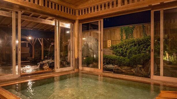 Un onsen japonais traditionnel, avec une architecture en bois, un bain en pierre et une vue sur le jardin environnant.