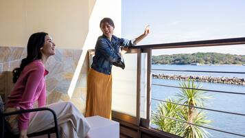 A room with a stone wall, a large window with a view of a body of water and a distant shoreline, and a person standing by the window.