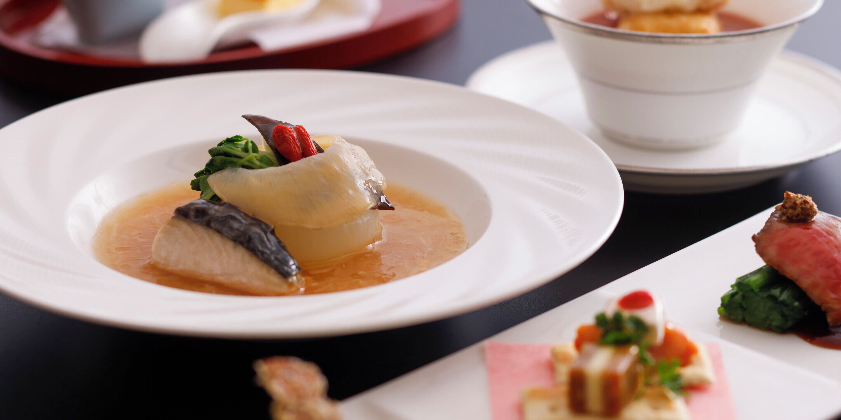 Uma mesa de jantar com pratos de comida, incluindo um prato de peixe com molho e legumes, e uma sobremesa com frutas e creme.