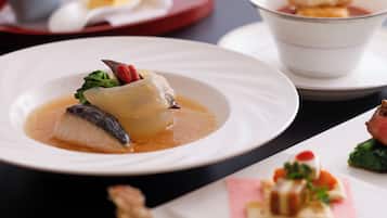 Uma mesa de jantar com pratos de comida, incluindo um prato de peixe com molho e legumes, e uma sobremesa com frutas e creme.