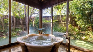 Un bain à remous dans une pièce fermée par des parois de verre, offrant une vue sur un jardin et une clôture en bois.