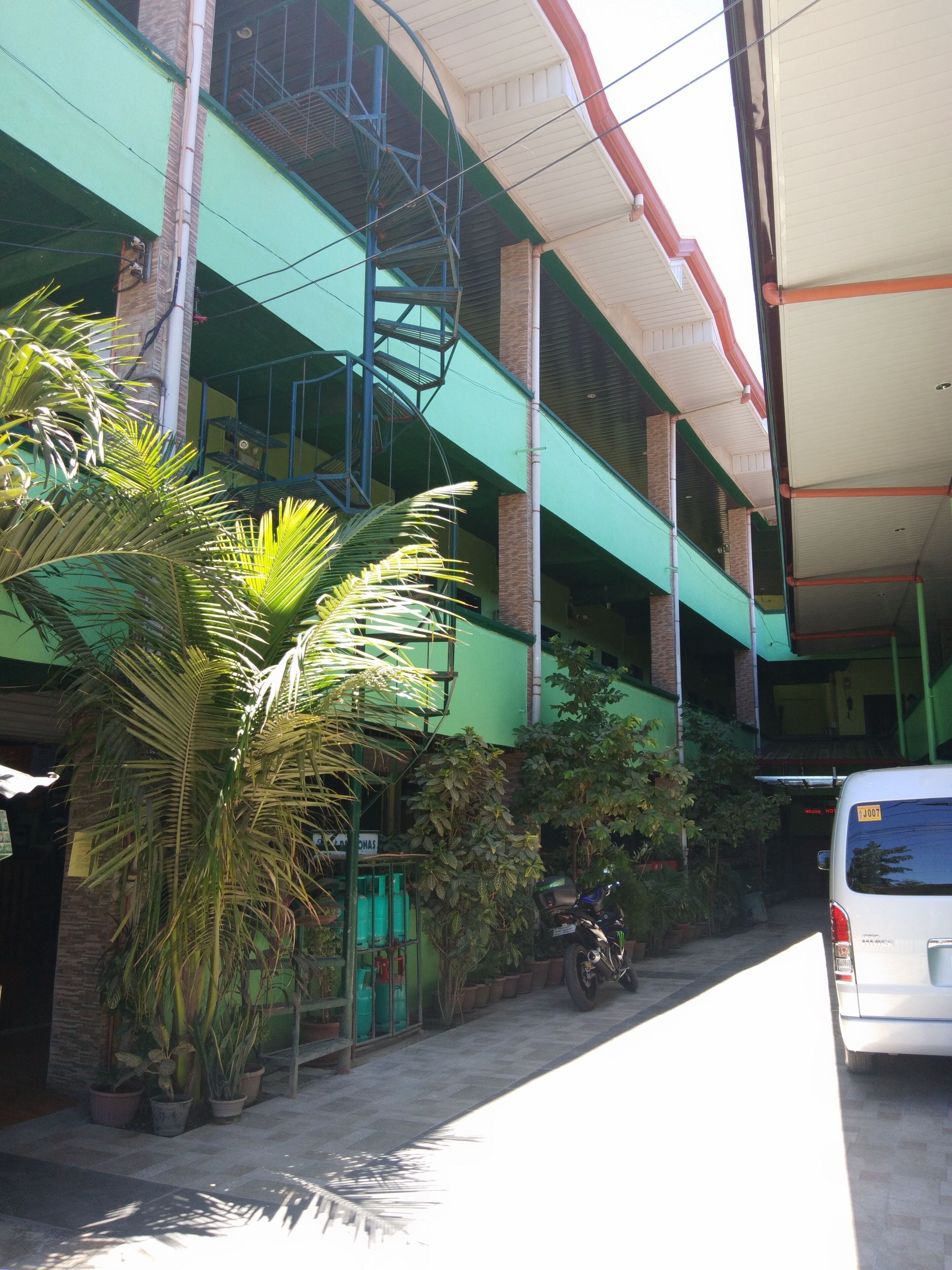 A multi-story building with a green facade, a staircase, and potted plants.