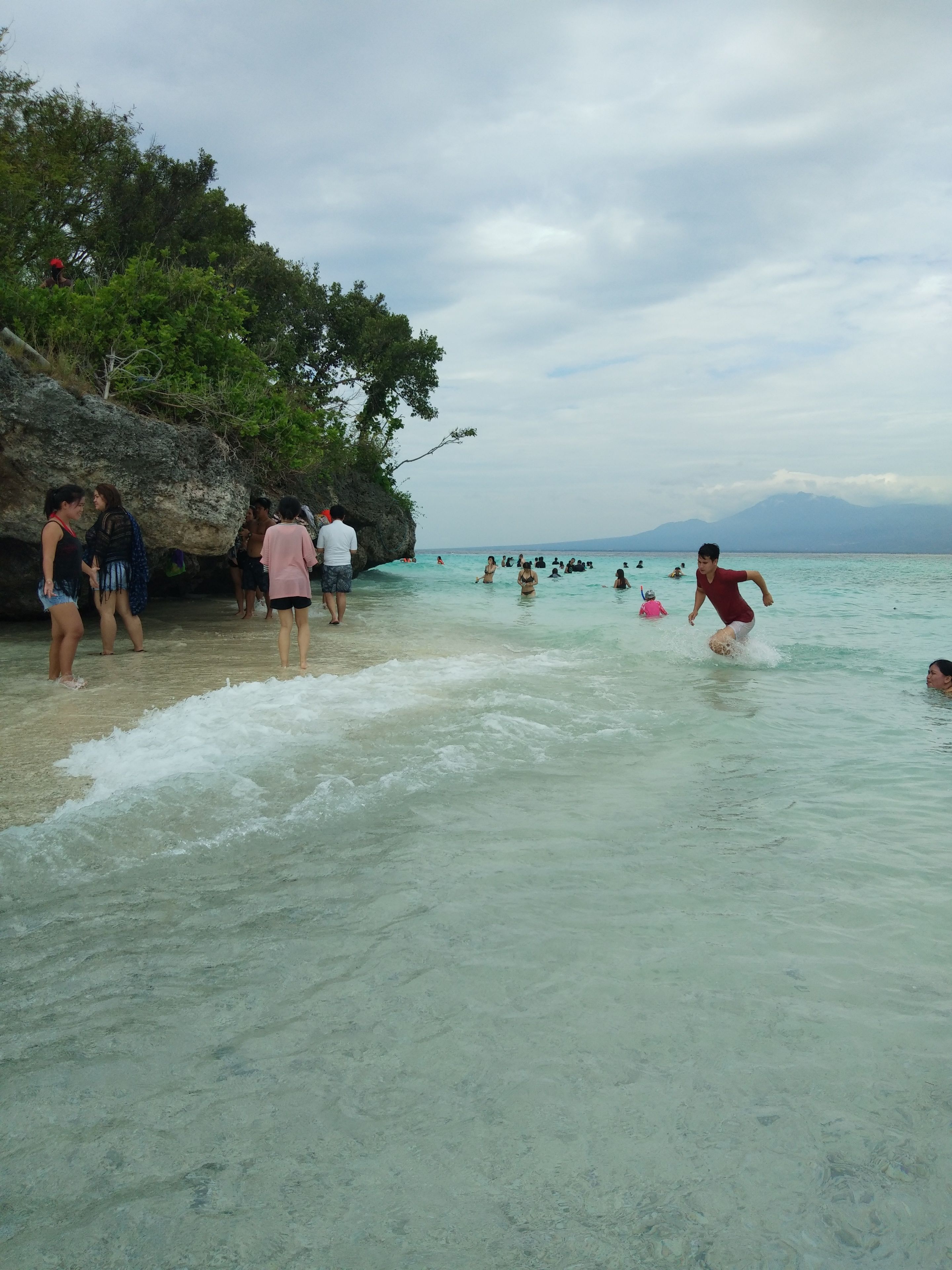 Una spiaggia con persone che nuotano e passeggiano sulla riva.