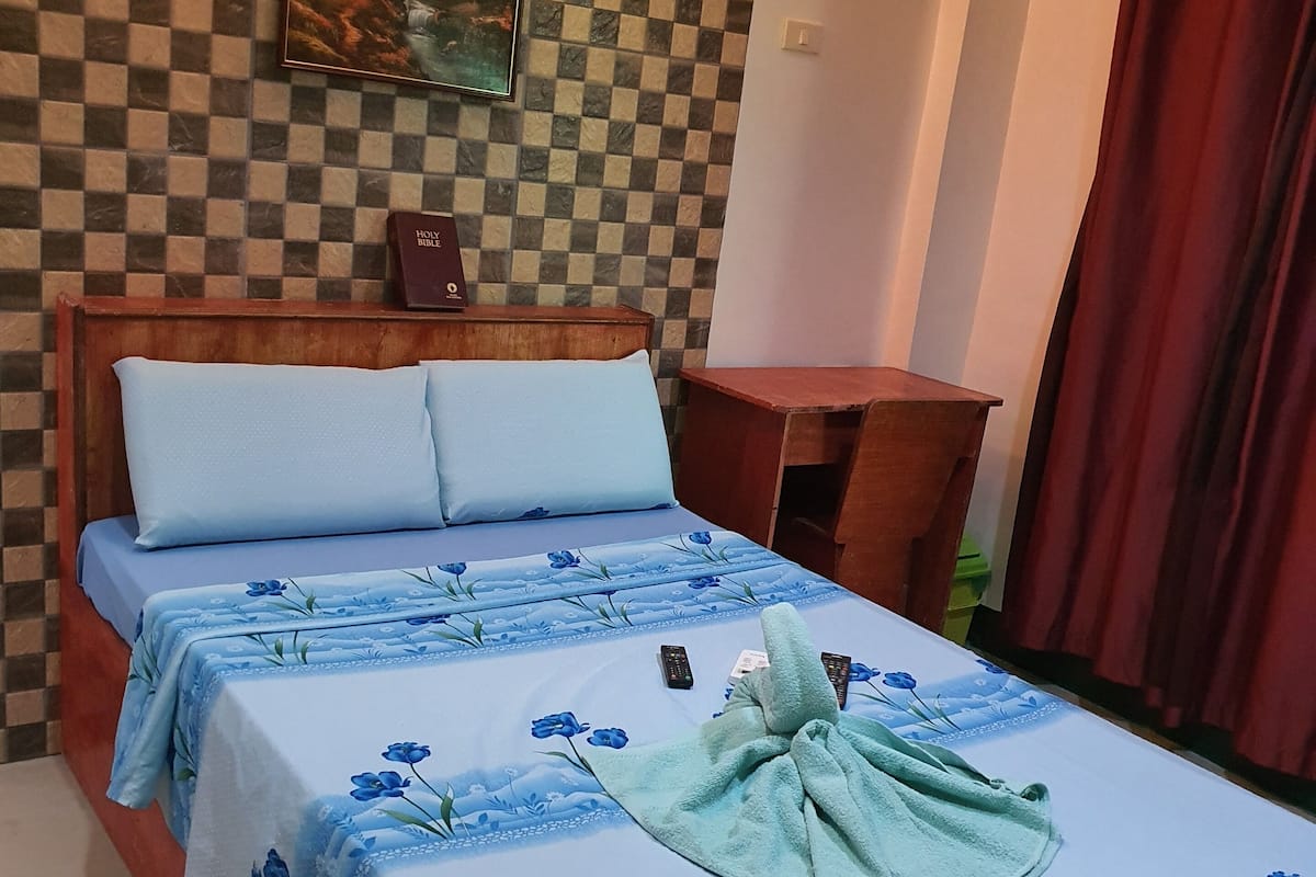 A neatly made bed with a floral bedspread, a headboard, and a wall-mounted painting above it.