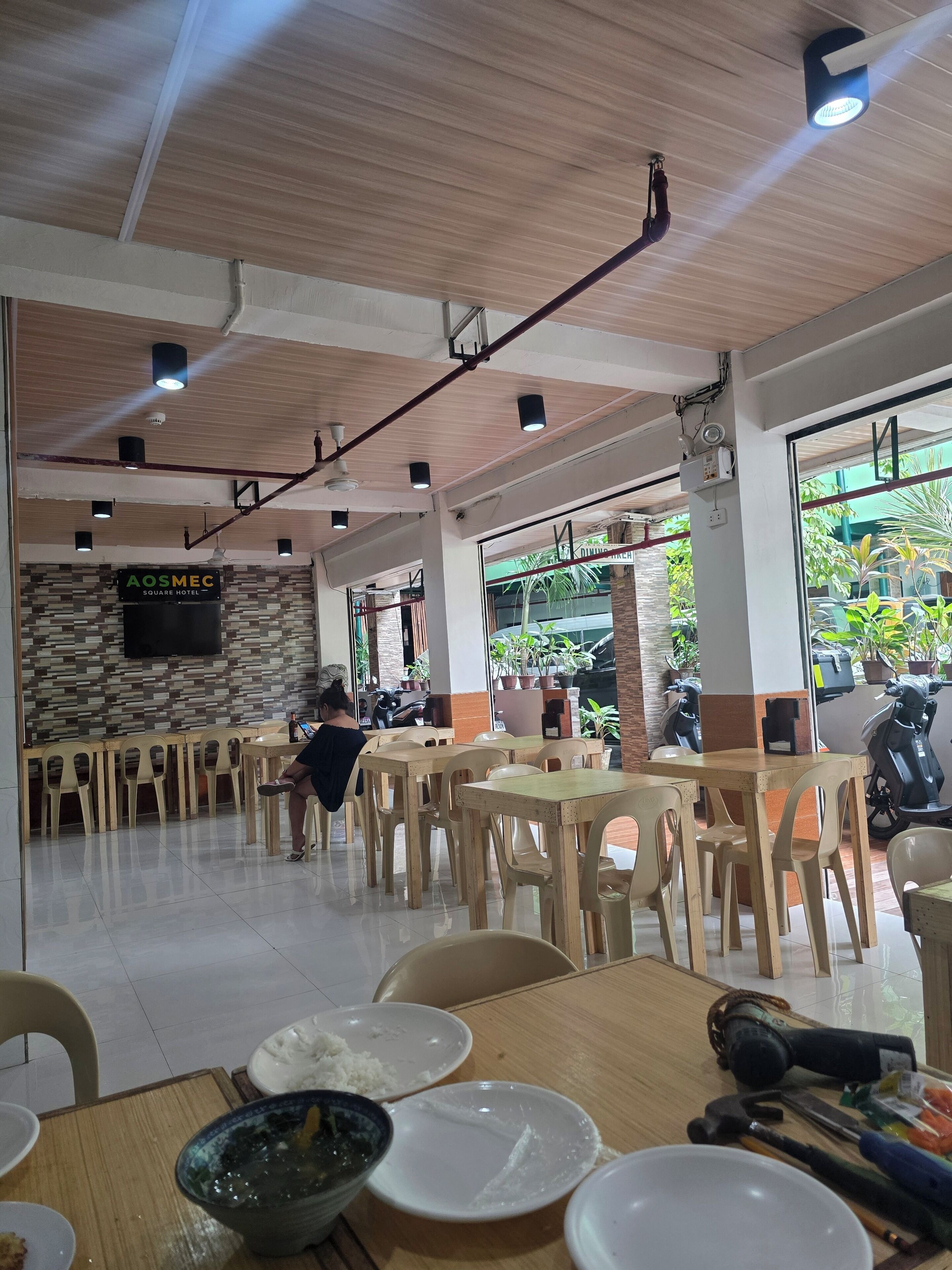 A spacious indoor area with multiple tables and chairs, a tiled floor, and a ceiling with exposed beams and lighting fixtures.