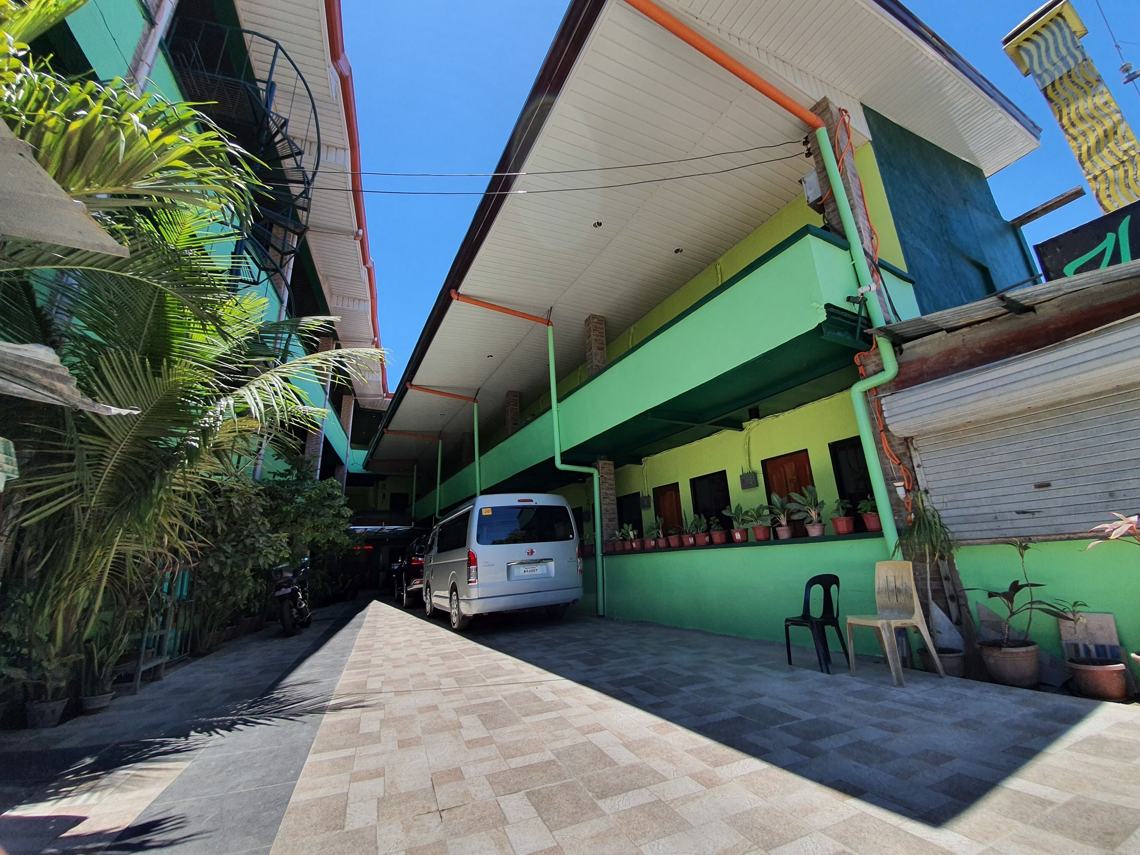 A narrow alleyway with a parked white van, potted plants, and a green building with a tiled floor.
