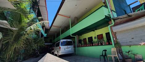 A narrow alleyway with a parked white van, potted plants, and a green building with a tiled floor.
