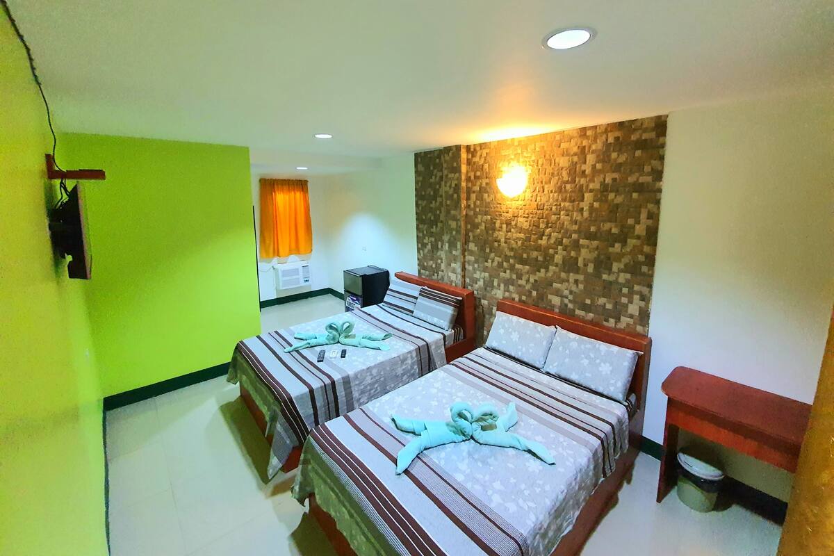 A hotel room with two beds, a small desk, a wall-mounted TV, and a wall-mounted light fixture.
