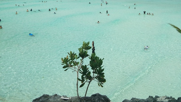 Ein Strand mit klarem türkisblauem Wasser und einem felsigen Vordergrund.