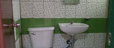 A bathroom with a toilet, sink, and green and white patterned walls.