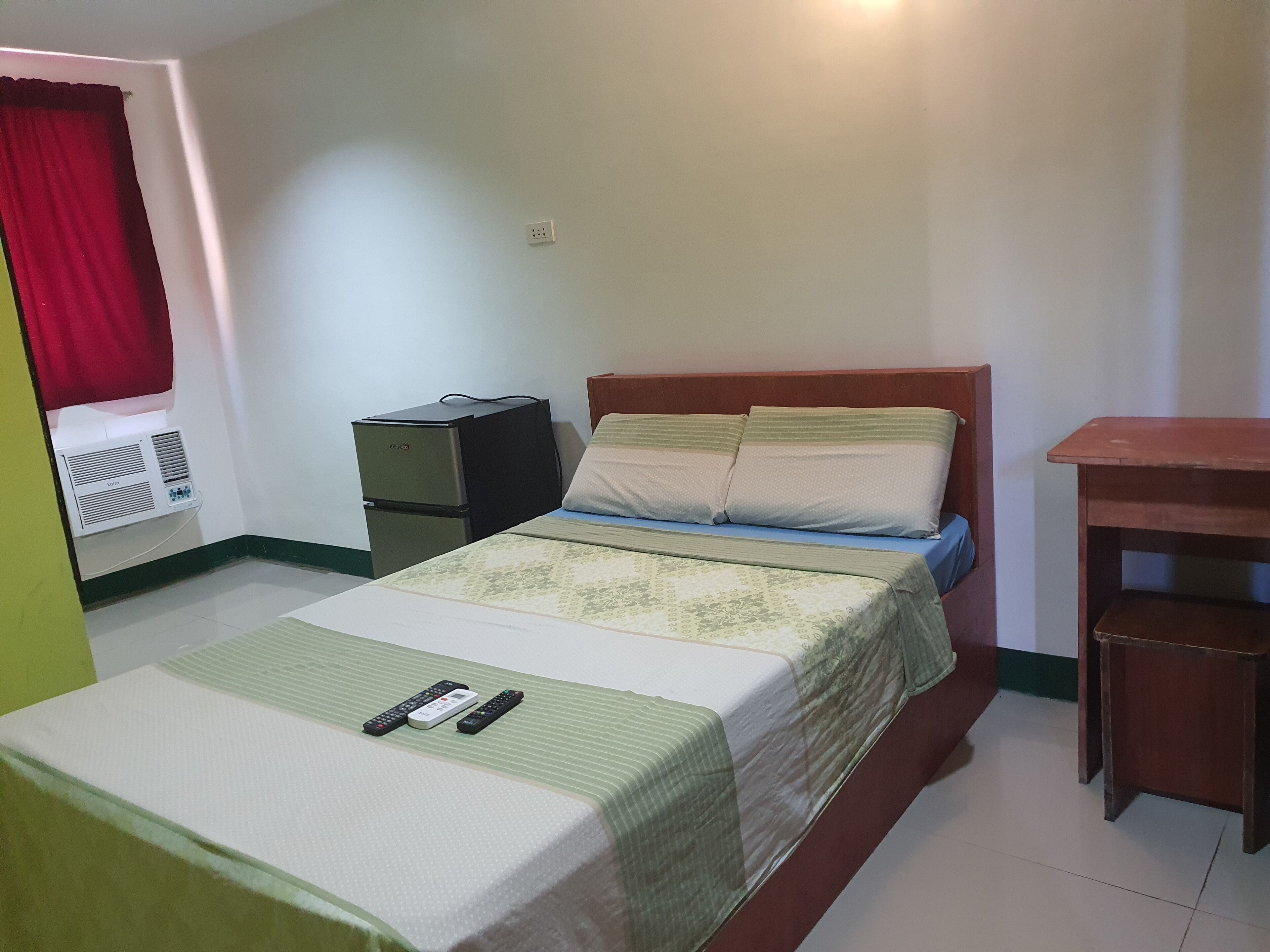A small, simple room with a bed, a nightstand, a heater, and a small table.