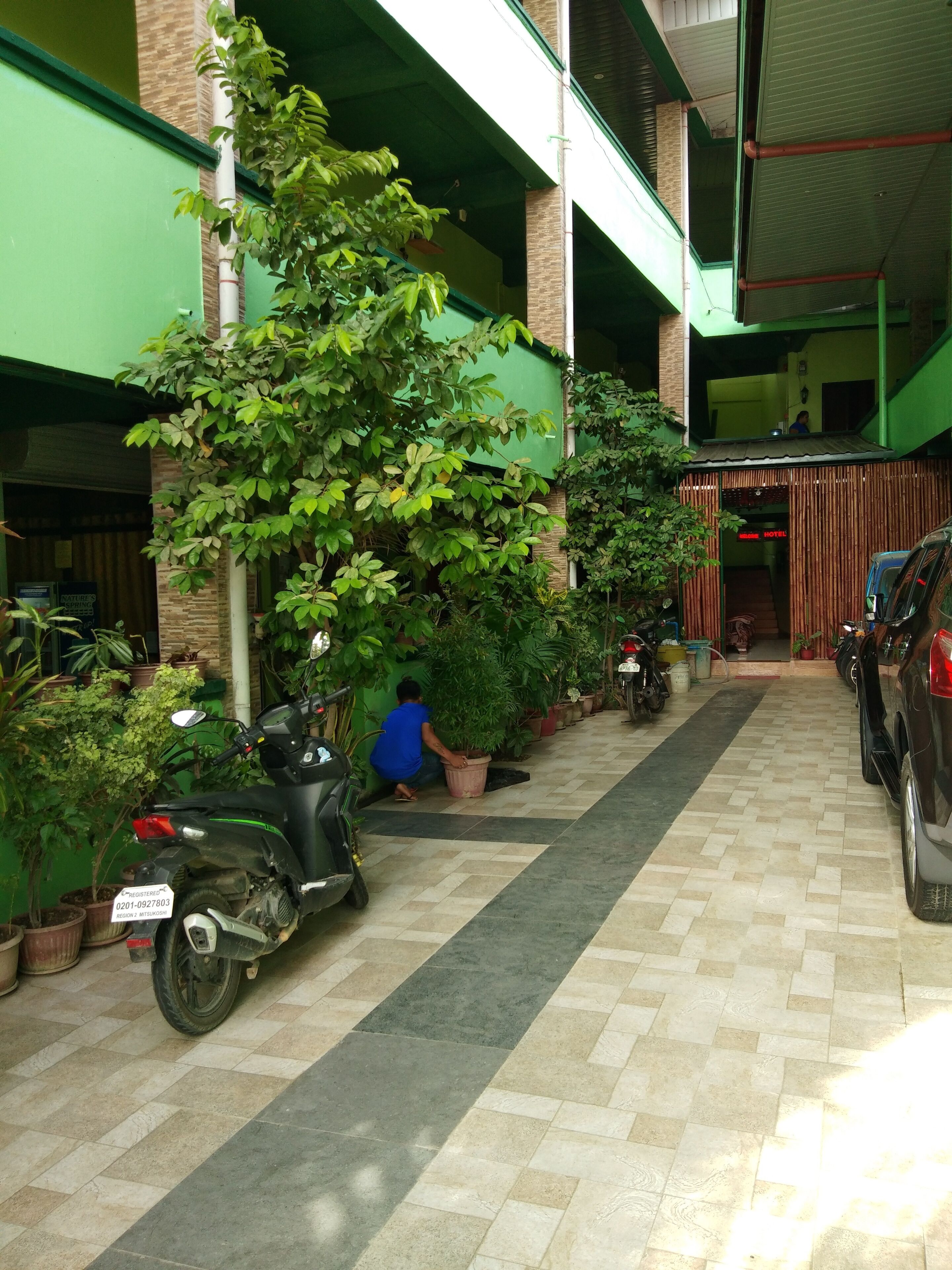 A covered outdoor area with potted plants, a scooter, and a car parked.