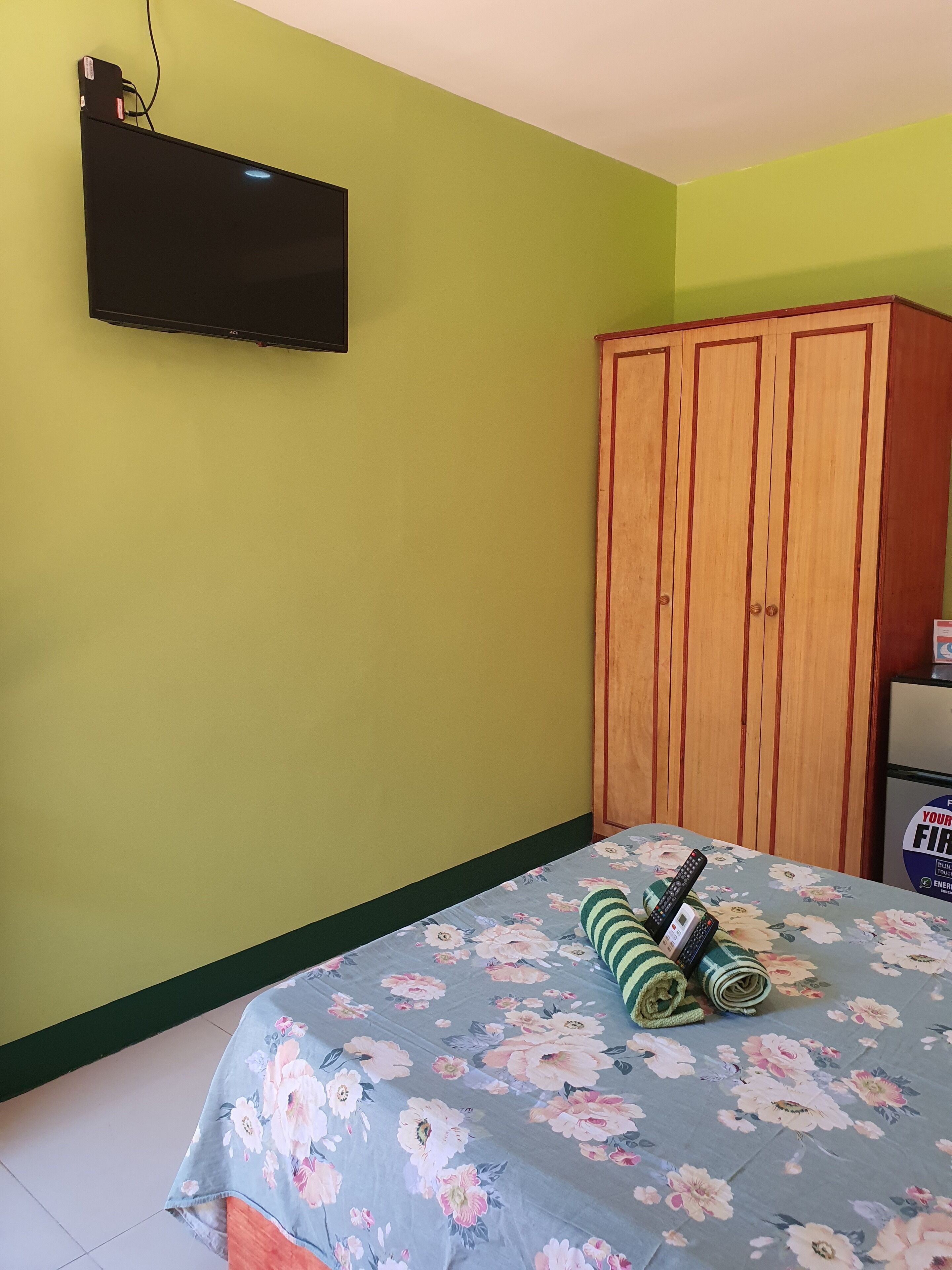 A room with a bed, a television mounted on the wall, and a wooden wardrobe.