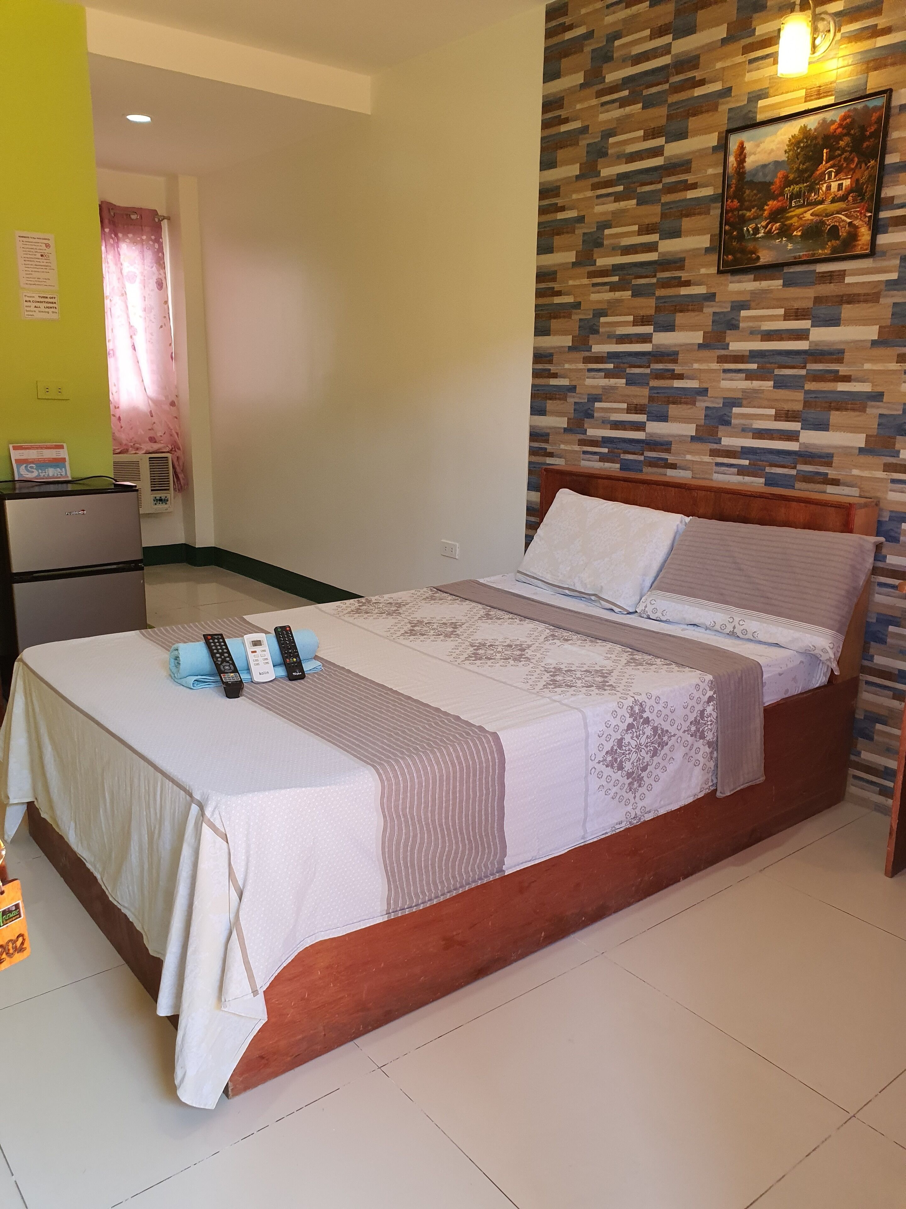 A neatly made bed with a patterned bedspread, a remote control, and a pillow on a wooden bed frame.