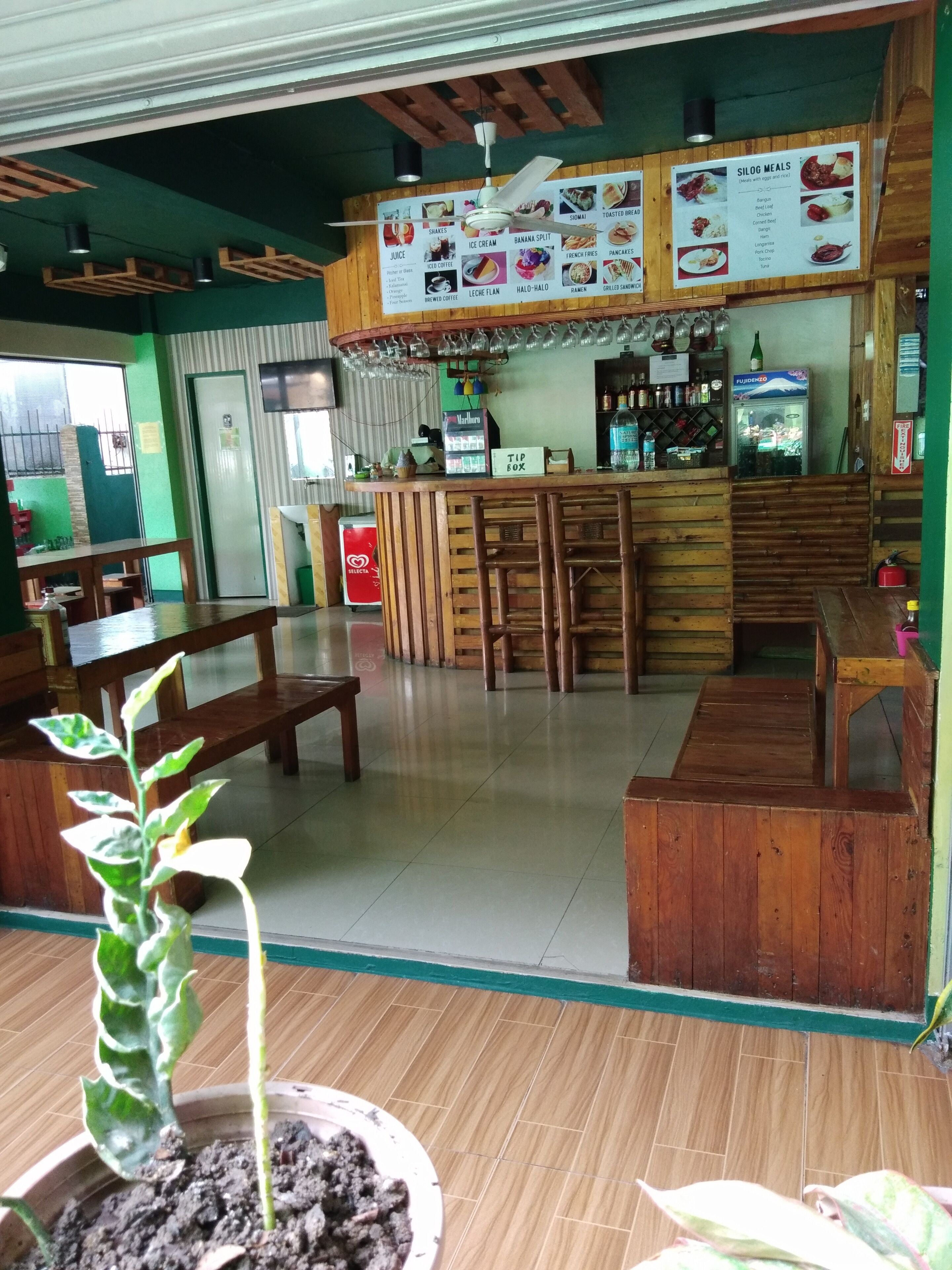 A restaurant interior with wooden furniture, a bar area, and a menu board displaying various food options.