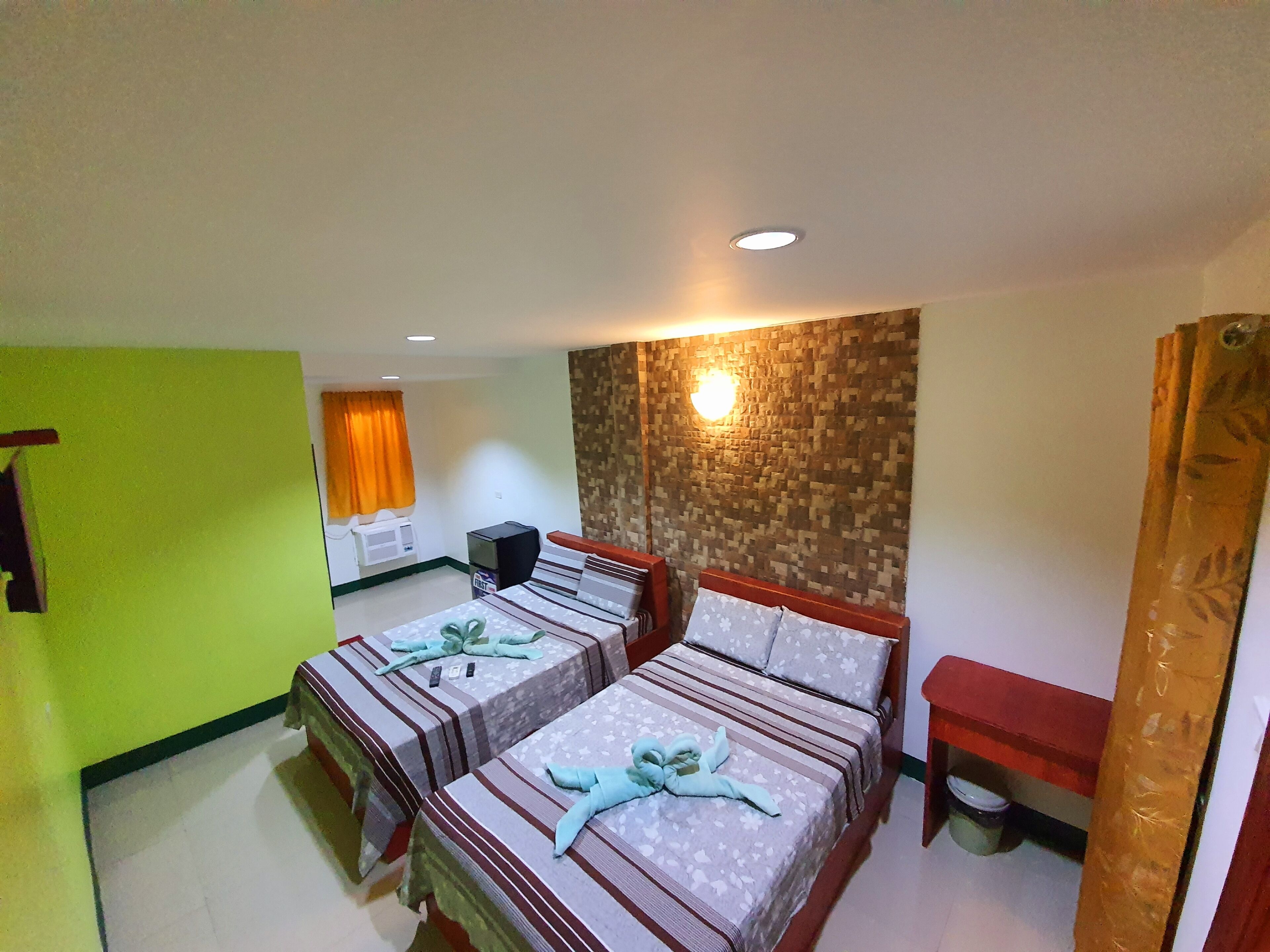 A hotel room with two beds, a small desk, a chair, and a wall-mounted light fixture.