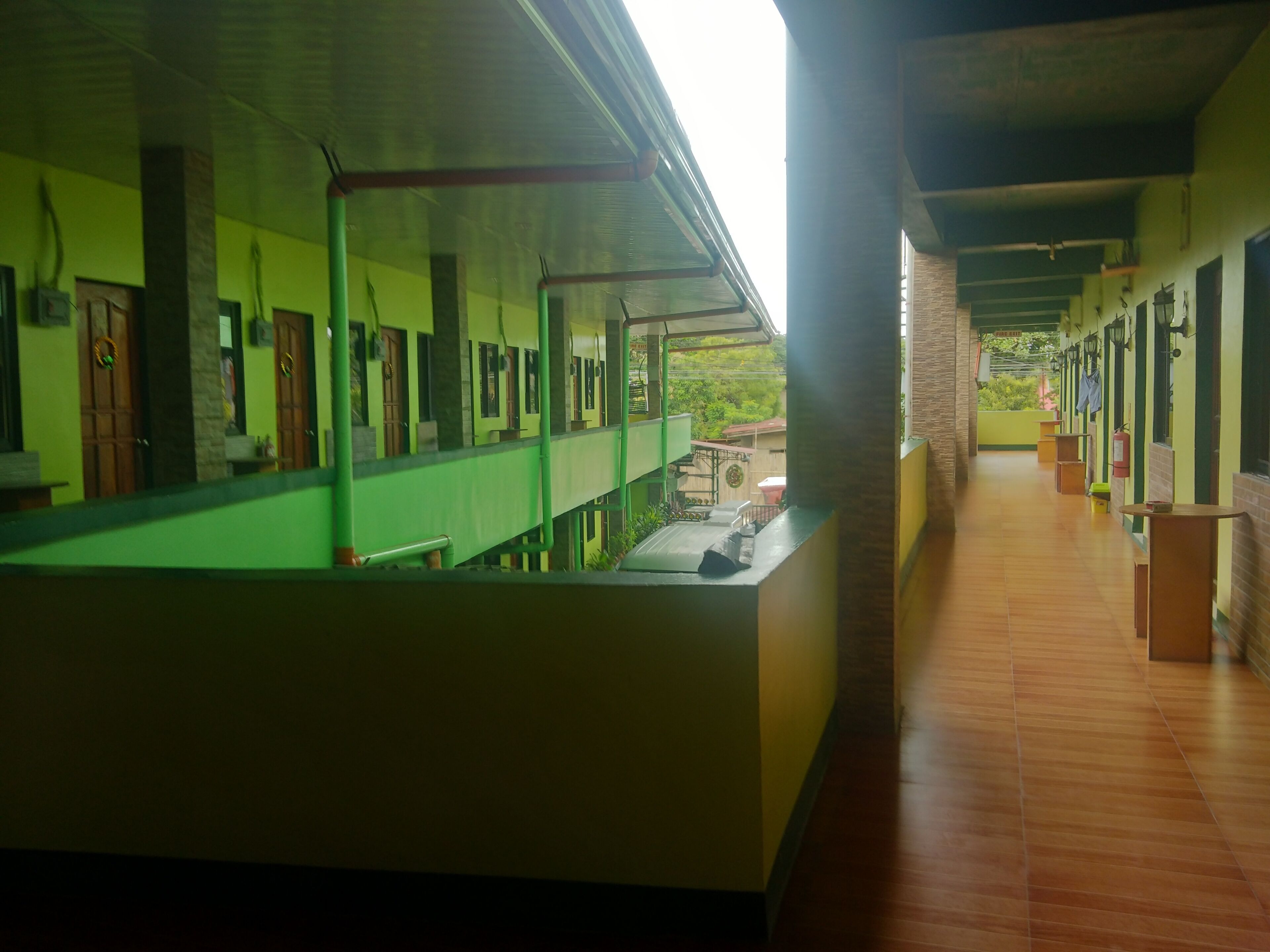 A corridor with a covered walkway, wooden flooring, and a view of greenery outside.