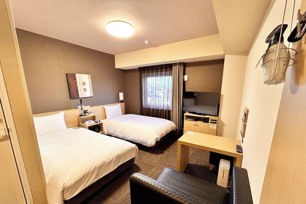 A hotel room with two beds, a desk, a TV, and a minibar.