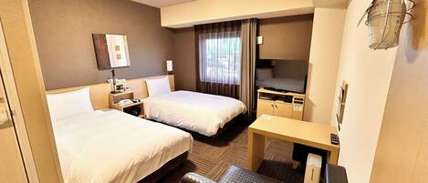 A hotel room with two beds, a desk, a TV, and a minibar.