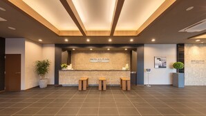 A reception area with a sign reading "HOTEL ROUTE INN," three wooden stools, a potted plant, and a tiled floor. - Hotel Route Inn Anan (Anan)