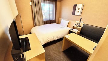 Una habitación de hotel con cama, mesita de noche, escritorio, silla, lámpara y ventana con cortinas.