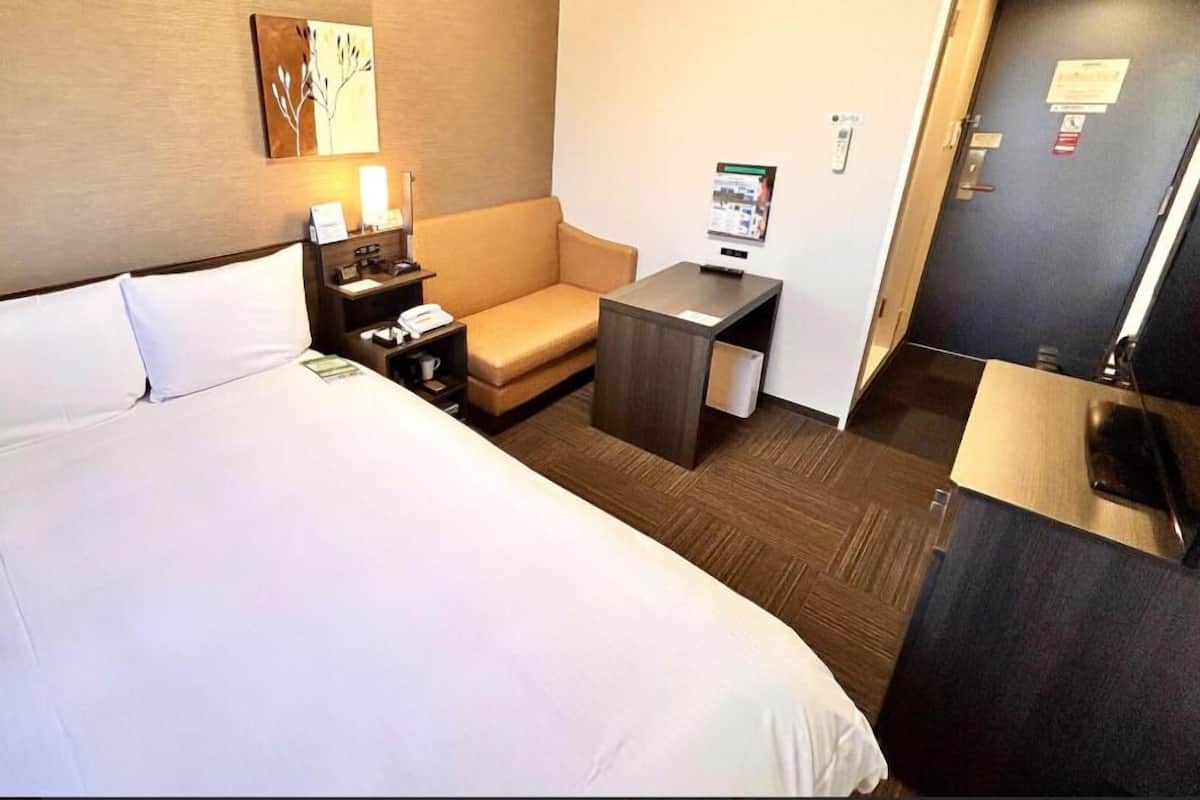 A hotel room with a large bed, a bedside table with a lamp, a small desk, and a sofa.
