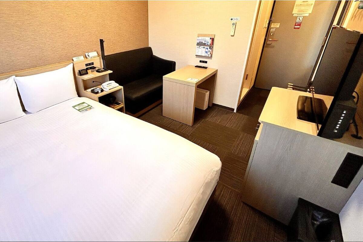 A hotel room with a large bed, a desk, a chair, a small table, and a TV.