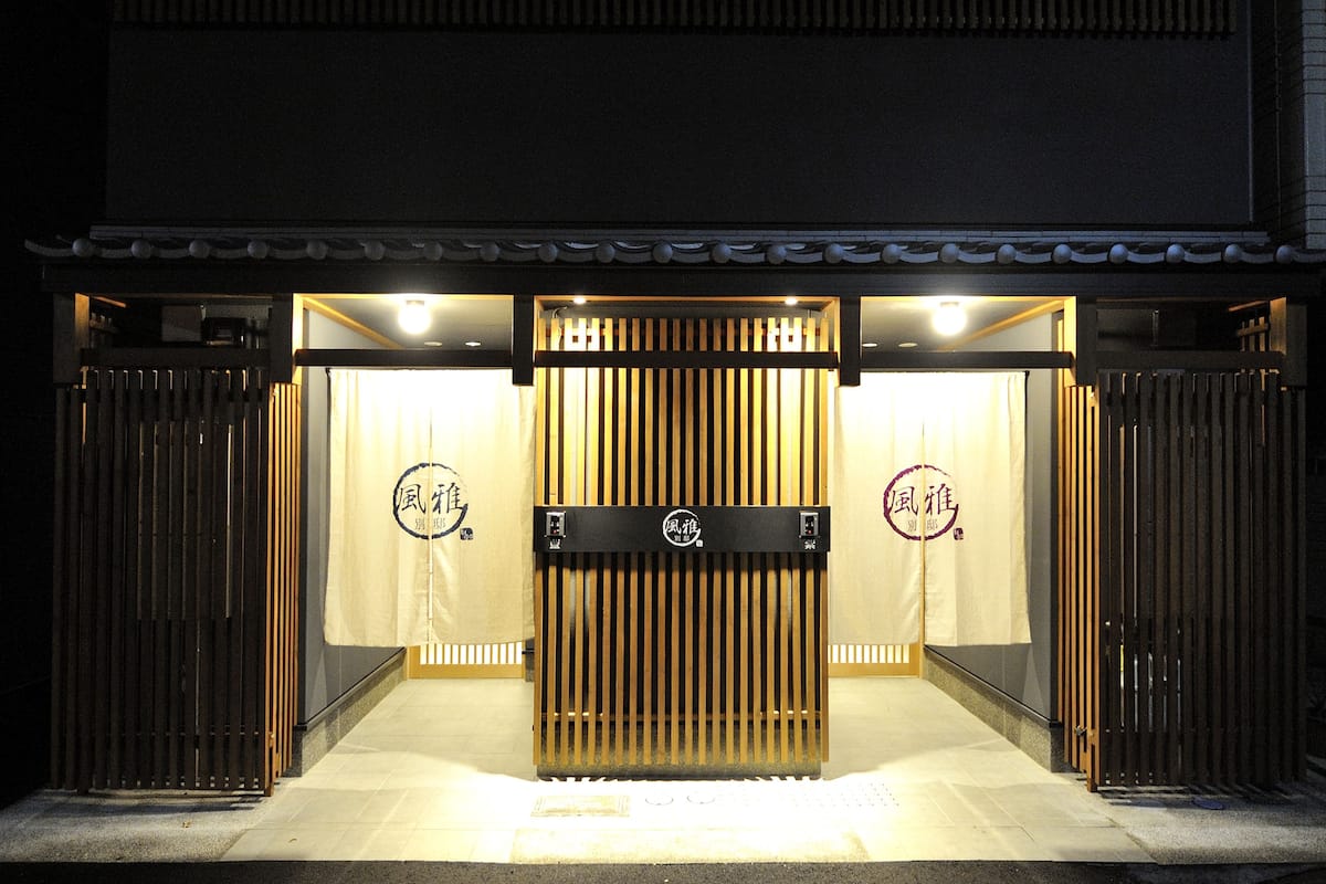 Il s'agit d'un bâtiment japonais traditionnel, doté d'une façade en bois, d'un portail d'entrée central et de deux enseignes lumineuses affichant des caractères japonais.