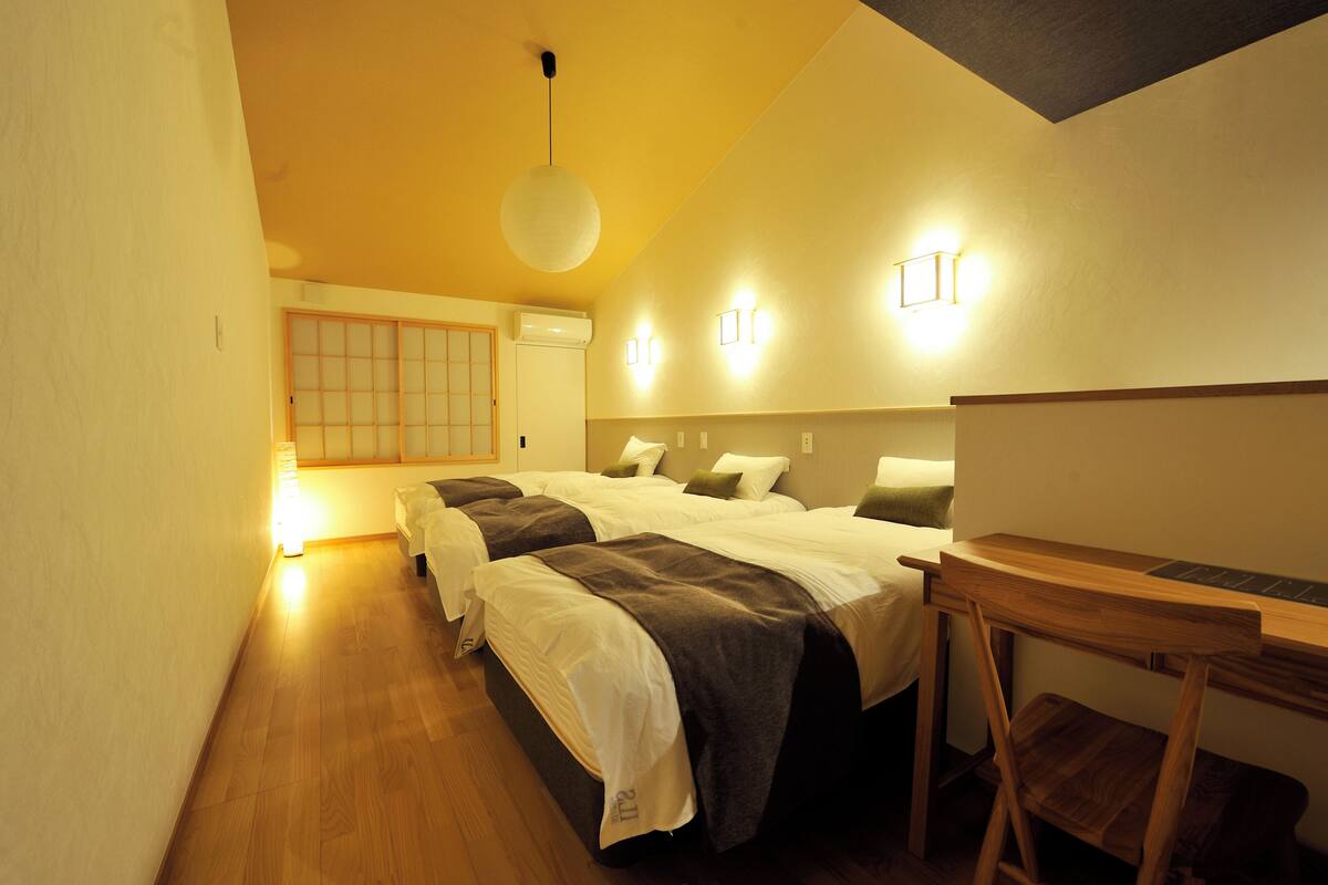 Une chambre d’hôtel avec deux lits, un bureau en bois et une porte coulissante de style japonais traditionnel.