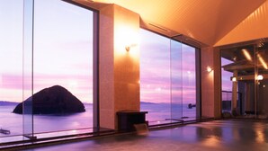 A spacious interior with large windows offering a view of a body of water and a distant island at sunset. - Kaisenkaku (Aomori)