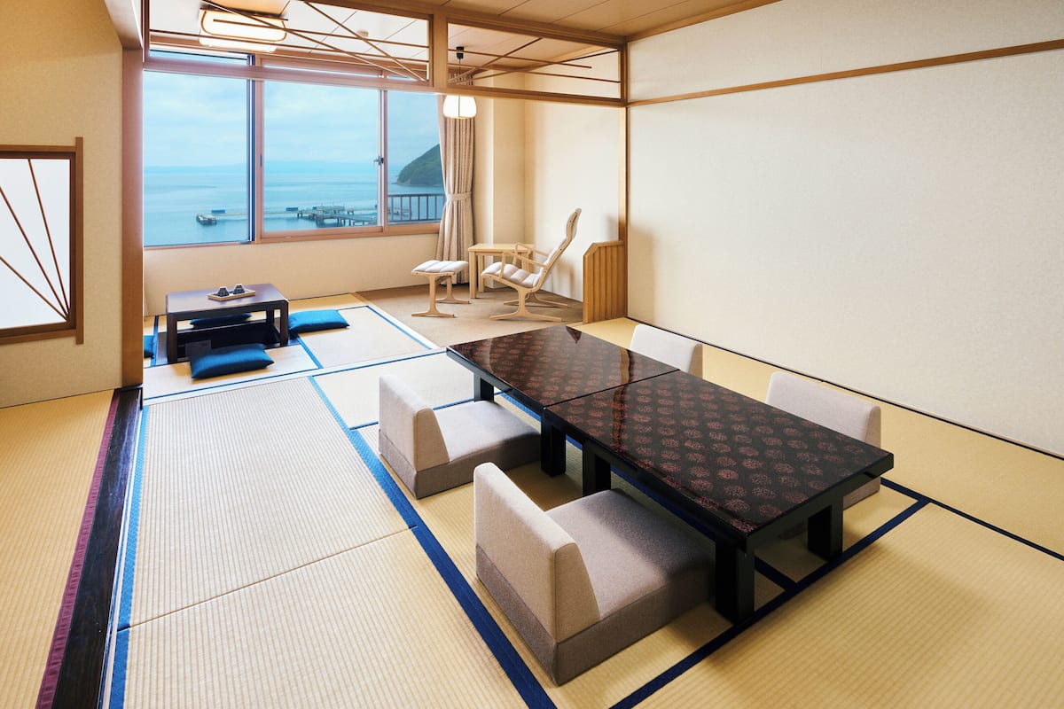 Tatami-mattoilla päällystetty huone, jossa on matala pöytä ja tuolit, suuret ikkunat, joista avautuu näkymä merelle, sekä perinteinen japanilaistyylinen katto.