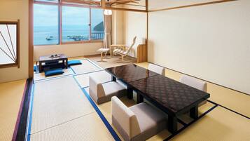 Ein Raum mit Tatami-Matten, einem niedrigen Tisch und Stühlen, mit Blick auf das Meer durch große Fenster und einer traditionellen japanischen Decke.