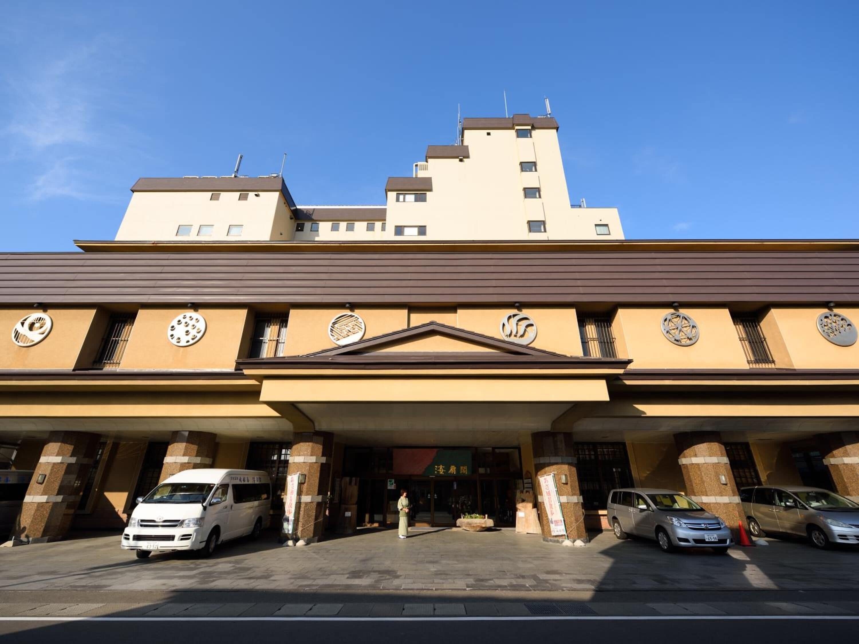 Fachada de hotel de diseño moderno, con entrada central que presenta un frontón triangular, amplias ventanas circulares y un techo plano.