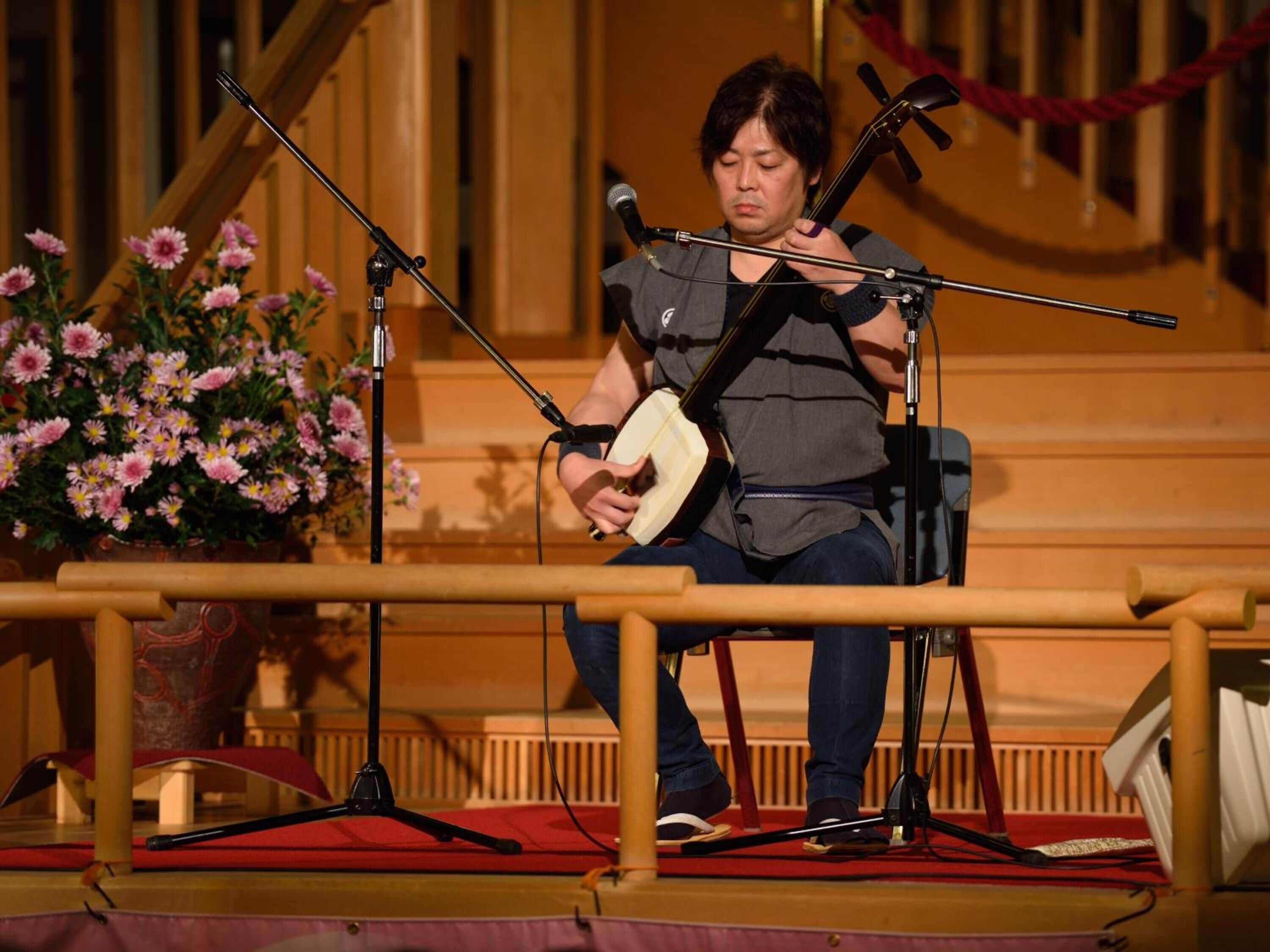 A person playing a stringed instrument on a stage with microphones and a floral arrangement.