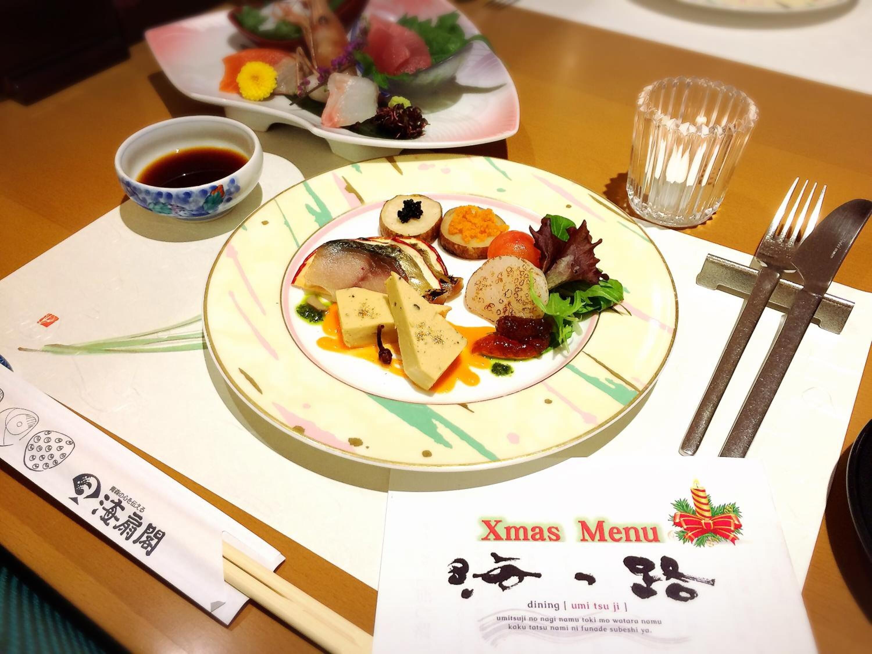 A table with a plate of sushi, a glass of water, chopsticks, a fork, and a menu with Japanese text.