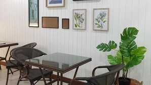 Una habitación con una mesa de vidrio y sillas de mimbre, una obra de arte en la pared y una planta grande en una cesta.