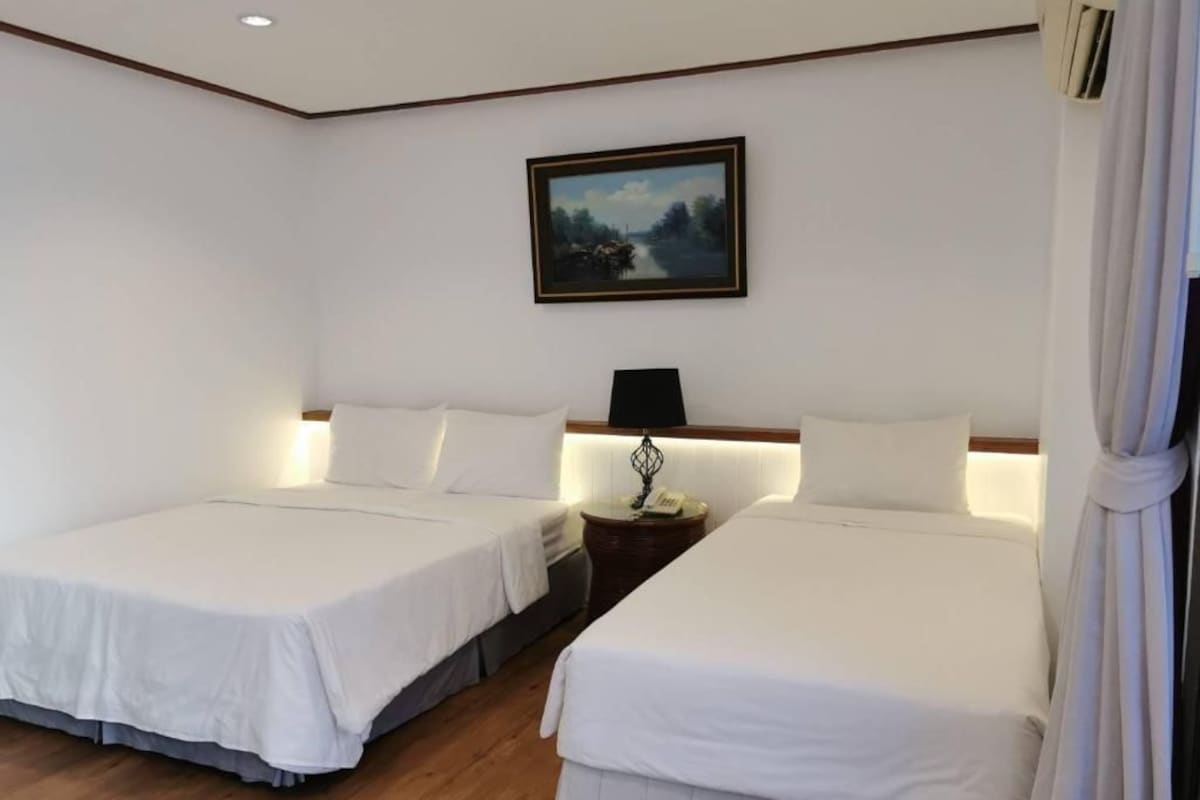 Een hotelkamer met twee bedden, een nachtkastje, een lamp en een schilderij aan de muur.