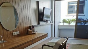 Una sala de estar moderna con piso de madera, un sofá, un televisor montado en la pared y un ventanal con vistas al exterior.