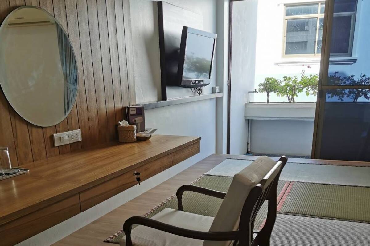 Ein modernes Wohnzimmer mit Holzboden, einer Couch, einem an der Wand montierten Fernseher und einem großen Fenster mit Blick nach draußen.