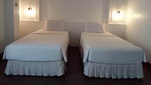 Dos camas individuales con ropa blanca y suelo oscuro, cada una con una lámpara de pared.
