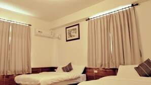 Ein Hotelzimmer mit zwei Einzelbetten, beigen Vorhängen, einem gerahmten Bild an der Wand und einer Klimaanlage.