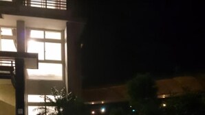 Nachtsicht auf ein Gebäude mit großen Fenstern und einem gepflasterten Weg, der zu einem kleinen Baum führt.