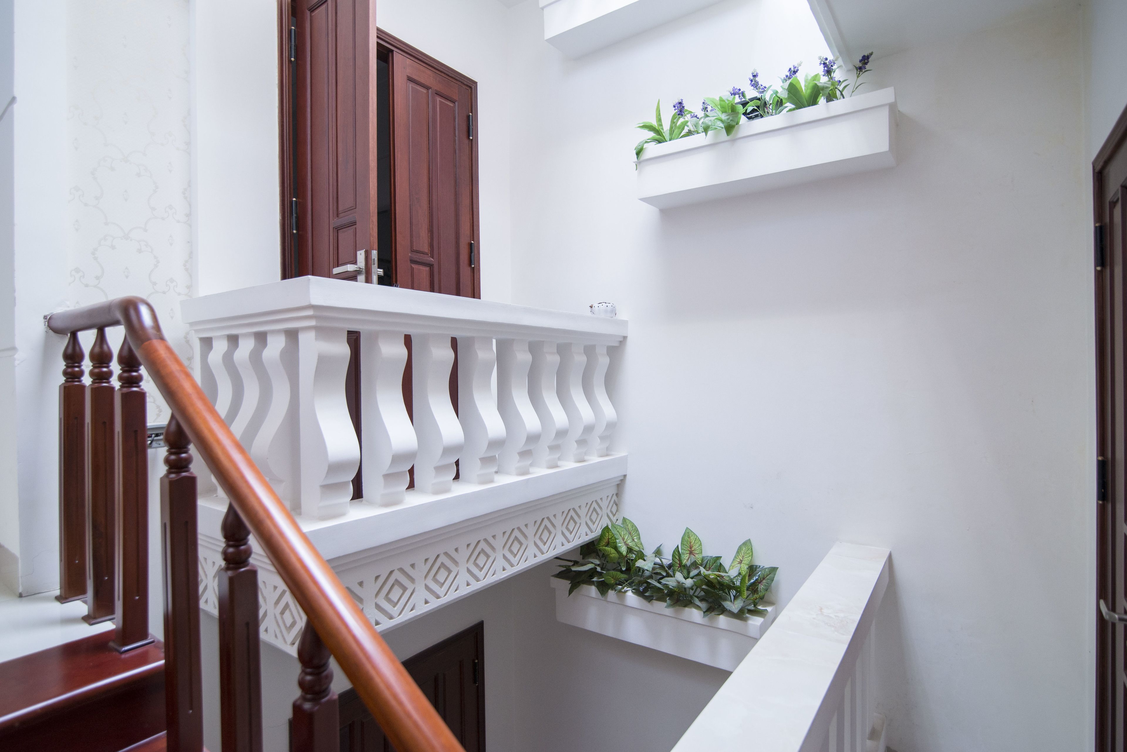 Una escalera con barandilla de madera y balaustrada blanca, que conduce a un rellano con una puerta de madera y una pared blanca con molduras decorativas.