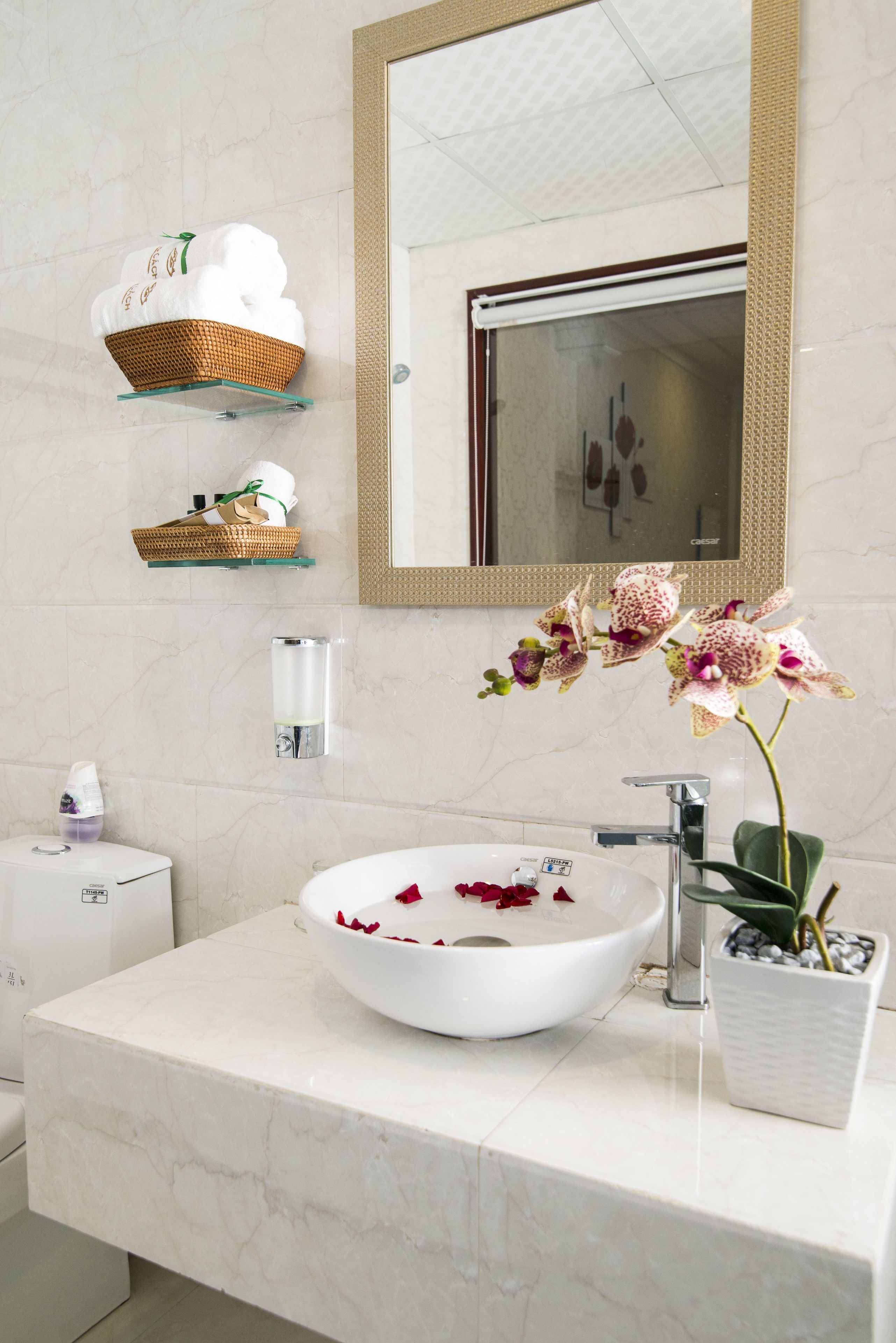 A bathroom with a white marble sink, a large mirror, a wicker basket with towels, and an orchid plant.