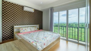 A bedroom with a checkered wall, a bed with floral bedding, an air conditioning unit, and a balcony with a view of greenery. - Platoo Pool Villa (Hua Hin)
