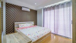 A bedroom with a checkered wall, a bed with floral bedding, an air conditioning unit, and a window with purple curtains. - Platoo Pool Villa (Hua Hin)