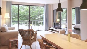 Camera d'albergo moderna con un ampio balcone, una zona pranzo con mobili in vimini e un televisore su un supporto in legno.