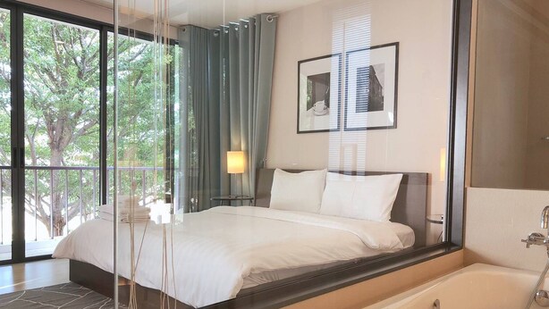 Camera d'albergo moderna con un ampio letto, una cabina doccia in vetro e vista sugli alberi dalle finestre.