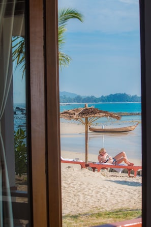A beach view with a wooden boat, a thatched umbrella, and a person relaxing on a bench.